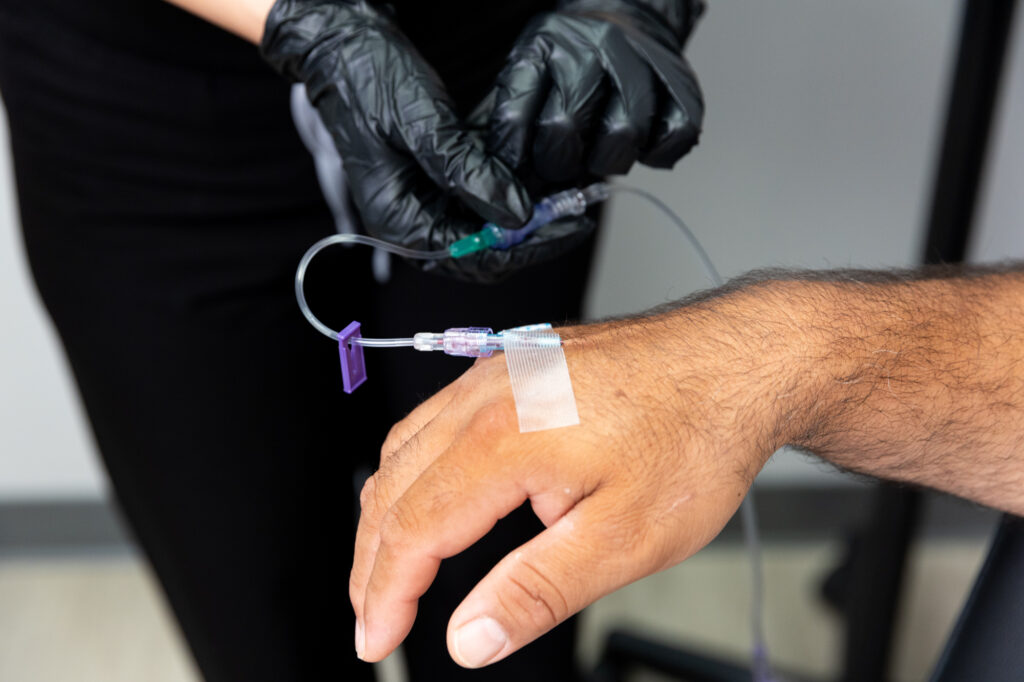 Provider wearing gloves inserts a needle attached to an IV drip in Jacksonville, NC into patient's vein. This therapy delivers vitamins and nutrients directly into the bloodstream.