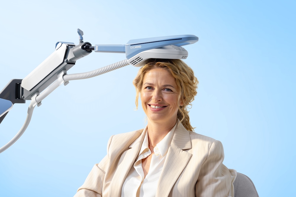 Woman smiles with ExoMind applicator placed on her head, this alternative treatment for depression in Jacksonville, NC, is comfortable and non-invasive.