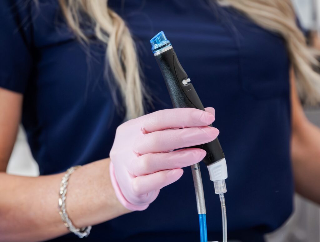 A medical provider wearing gloves holds the handheld HydraFacial device, preparing it for use during a professional facial in Jacksonville, NC. This service can be customized to the patient's specific skincare goals and can improve wrinkles, dryness, dull skin, and more.
