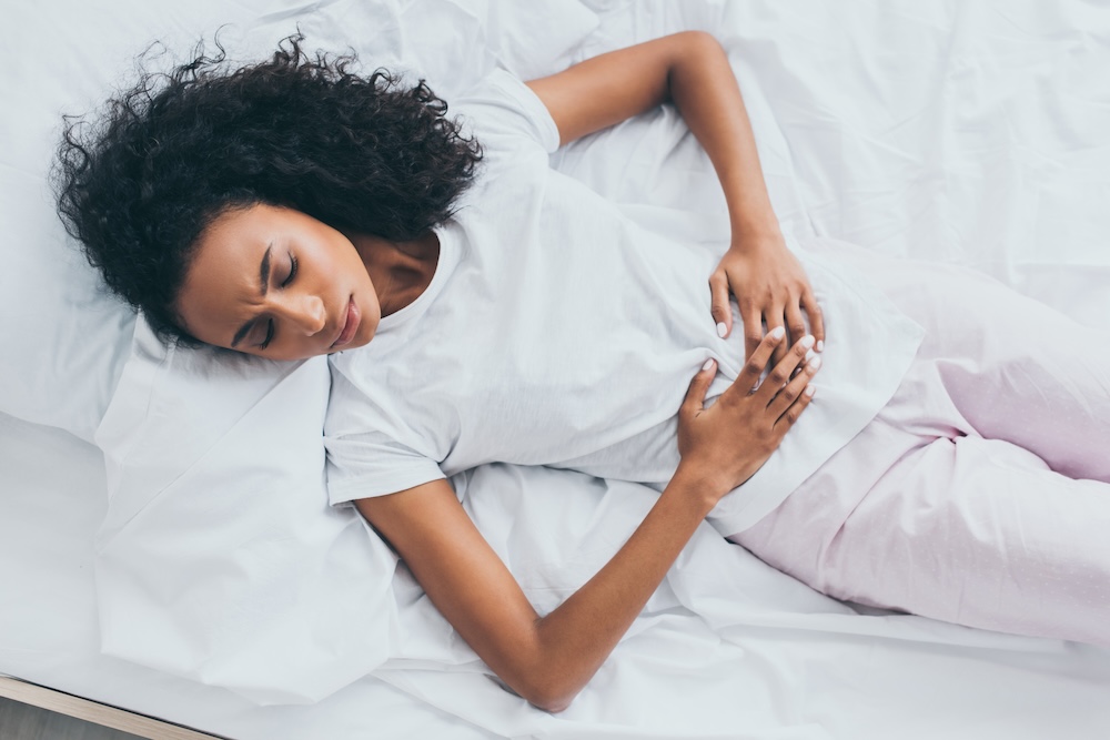 Woman lays in bed and holds her stomach while considering seeing a doctor for menstrual pain relief in Jacksonville, NC.