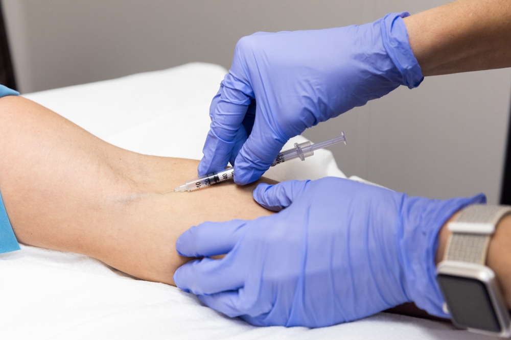 Provider wearing gloves places needle into patient's arm to attach to an IV drip. The patient is receiving IV therapy for immunity in Jacksonville, NC.