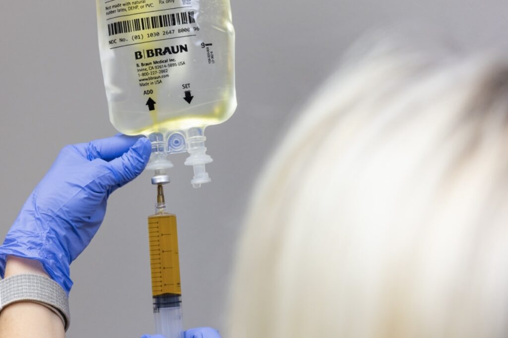 Provider wearing gloves connects IV infusion bag to tube. This is part of a series of treatments for immune support in Jacksonville, NC.